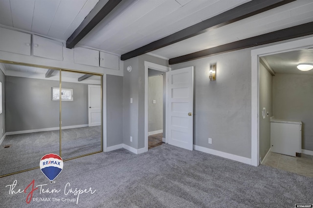 unfurnished bedroom featuring beamed ceiling, a closet, and light carpet