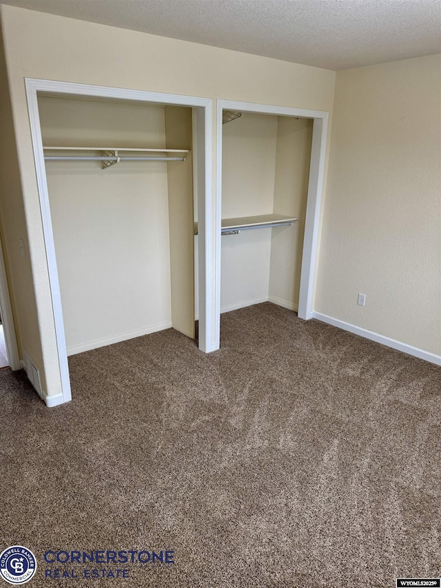 unfurnished bedroom featuring two closets, a textured ceiling, and dark colored carpet