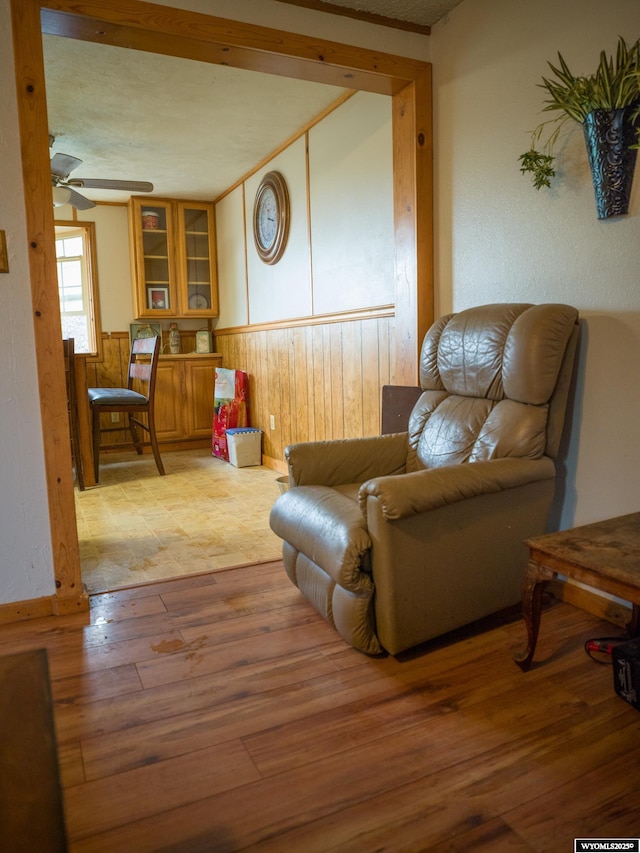 sitting room featuring wood walls, ceiling fan, and light wood-type flooring