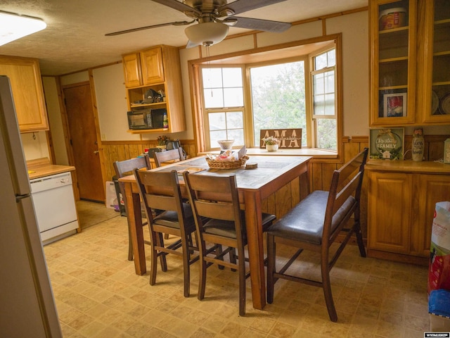 dining space featuring ceiling fan, a textured ceiling, and wood walls