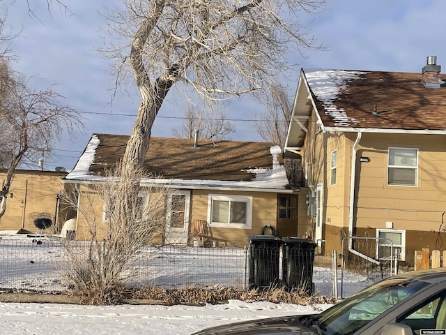 snow covered back of property featuring a fenced front yard and roof with shingles