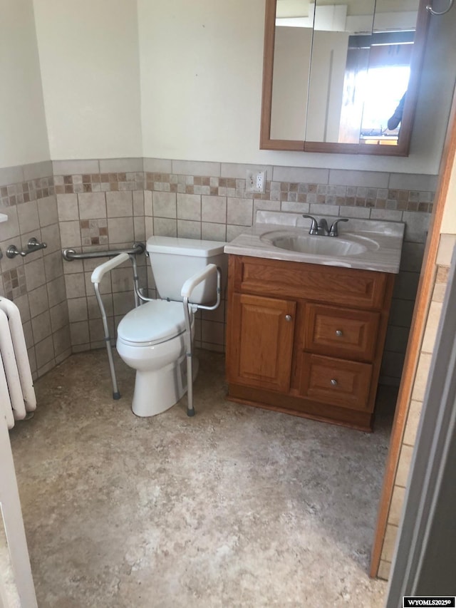 half bath with toilet, a wainscoted wall, tile walls, and vanity