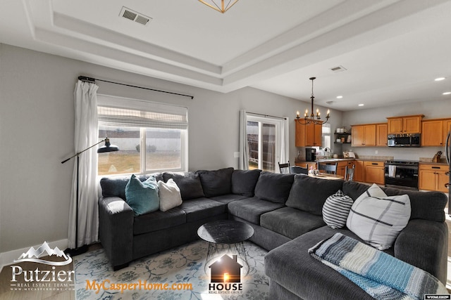 living room with sink, a tray ceiling, and a chandelier