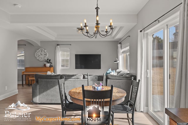 dining room featuring an inviting chandelier, a raised ceiling, and light hardwood / wood-style floors