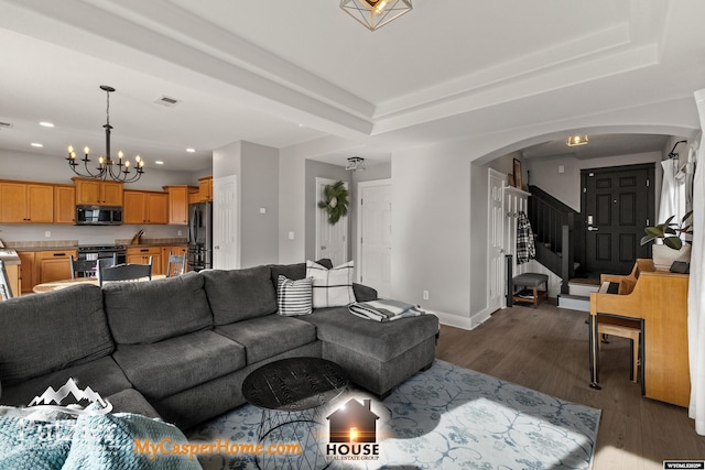 living room featuring dark wood-type flooring, a tray ceiling, and a chandelier