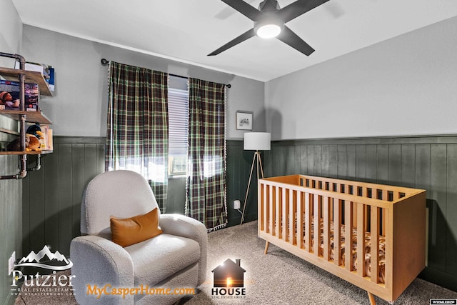 carpeted bedroom with a crib and ceiling fan