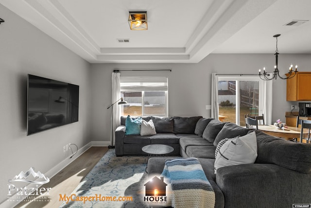 living room with hardwood / wood-style flooring, a tray ceiling, and a notable chandelier