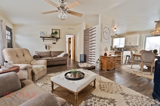 living room featuring ceiling fan with notable chandelier, a textured ceiling, and dark hardwood / wood-style flooring