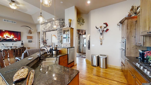 kitchen with appliances with stainless steel finishes, sink, light hardwood / wood-style flooring, dark stone counters, and hanging light fixtures