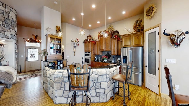 kitchen featuring appliances with stainless steel finishes, hanging light fixtures, a breakfast bar area, light hardwood / wood-style floors, and backsplash