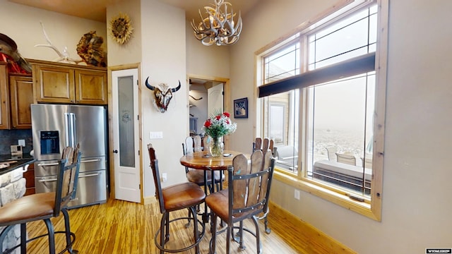 kitchen with an inviting chandelier, light hardwood / wood-style flooring, backsplash, stainless steel refrigerator with ice dispenser, and a high ceiling