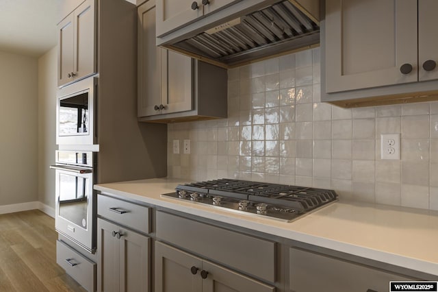 kitchen featuring gray cabinets, appliances with stainless steel finishes, tasteful backsplash, and custom range hood