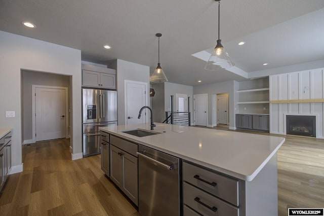 kitchen featuring appliances with stainless steel finishes, a center island with sink, pendant lighting, gray cabinets, and sink