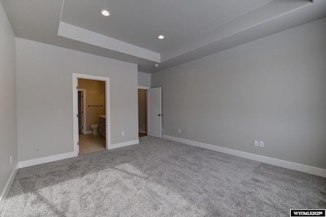 unfurnished bedroom with light carpet, a tray ceiling, and connected bathroom