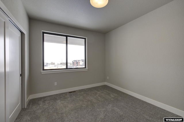 unfurnished bedroom featuring a textured ceiling, a closet, and dark carpet