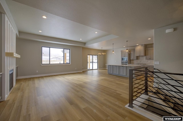 unfurnished living room featuring a raised ceiling, light hardwood / wood-style flooring, sink, and an inviting chandelier