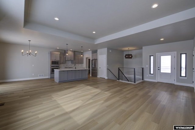 unfurnished living room with a raised ceiling, light hardwood / wood-style floors, sink, and a notable chandelier