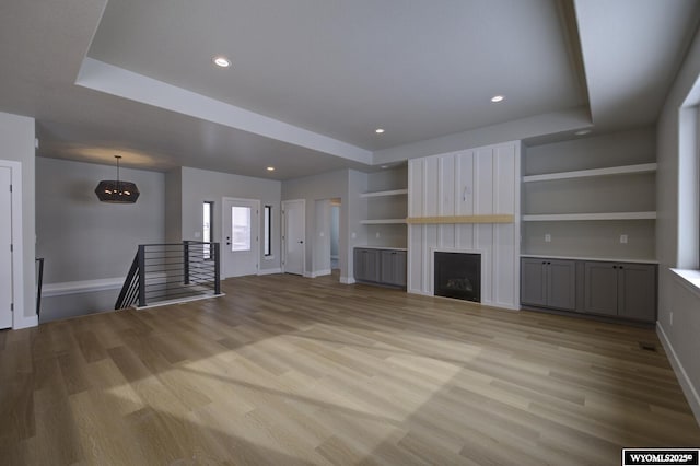 unfurnished living room featuring a tray ceiling, a large fireplace, light hardwood / wood-style floors, and built in features