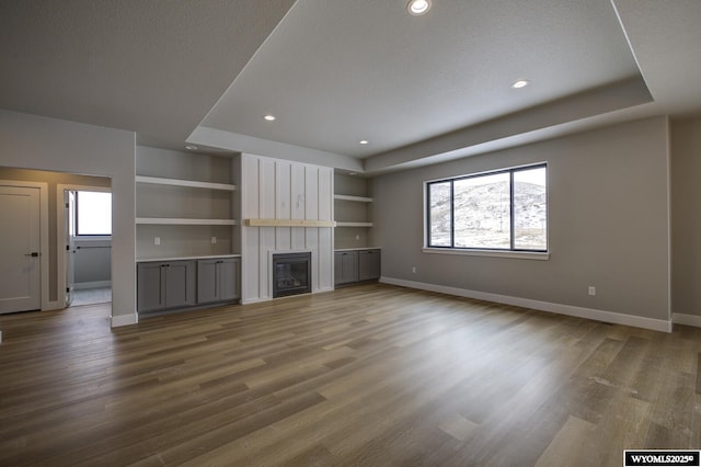 unfurnished living room with a tray ceiling, built in shelves, wood-type flooring, and a textured ceiling