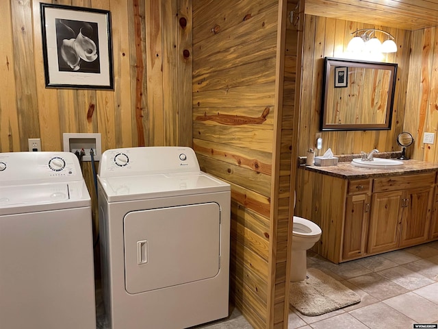 laundry area with independent washer and dryer, light tile patterned floors, wooden walls, and sink