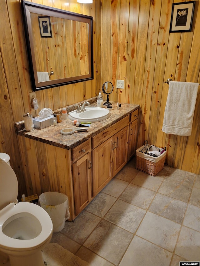 bathroom with toilet, vanity, and wooden walls