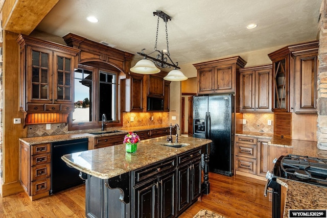 kitchen with a center island with sink, pendant lighting, sink, and black appliances