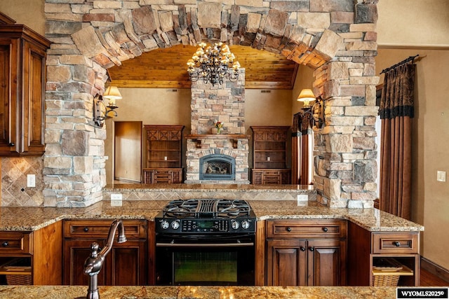 kitchen with a fireplace, backsplash, black gas range oven, and light stone counters