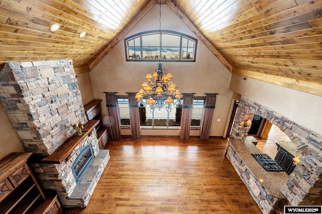 unfurnished living room featuring hardwood / wood-style flooring, an inviting chandelier, a stone fireplace, and wood ceiling