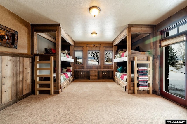 carpeted bedroom featuring a textured ceiling, access to outside, and wood walls