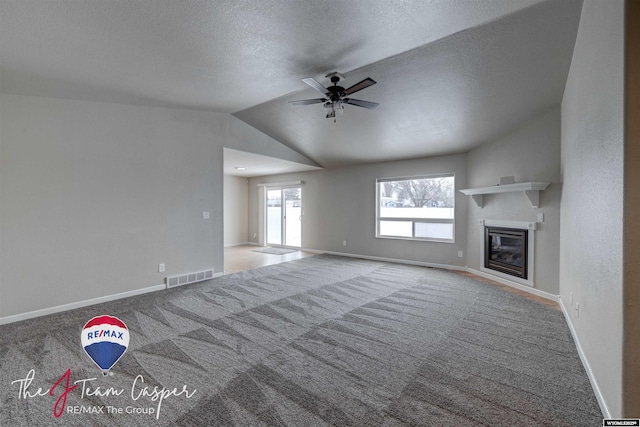 unfurnished living room featuring lofted ceiling, ceiling fan, carpet flooring, and a textured ceiling