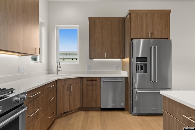 kitchen with light countertops, appliances with stainless steel finishes, a sink, and light wood-style flooring