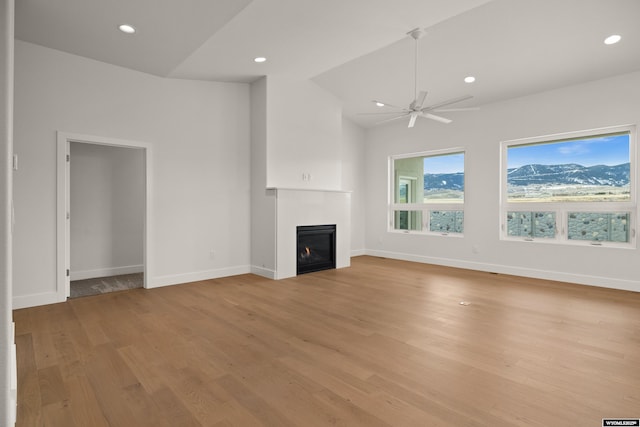 unfurnished living room featuring lofted ceiling, recessed lighting, baseboards, light wood-style floors, and a glass covered fireplace