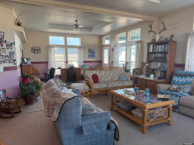 carpeted living room with ceiling fan, plenty of natural light, and a raised ceiling