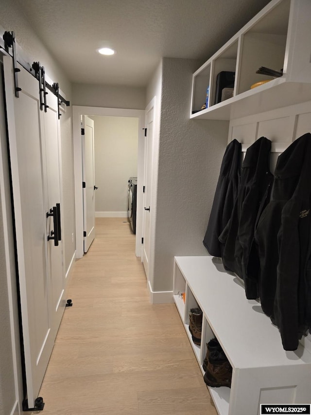 mudroom with a textured wall, a barn door, washing machine and dryer, baseboards, and light wood-type flooring