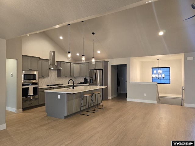 kitchen with stainless steel appliances, gray cabinets, light countertops, an inviting chandelier, and wall chimney range hood