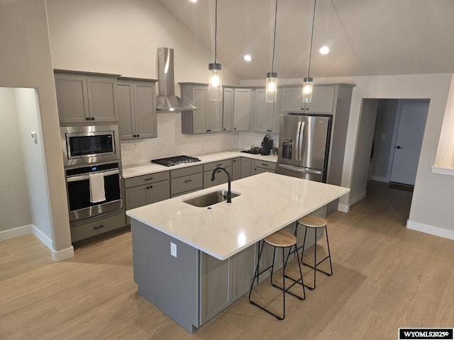 kitchen with light wood finished floors, appliances with stainless steel finishes, gray cabinets, wall chimney range hood, and a sink