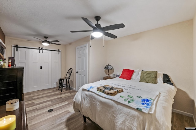 bedroom featuring a barn door, a textured ceiling, wood-type flooring, and a closet