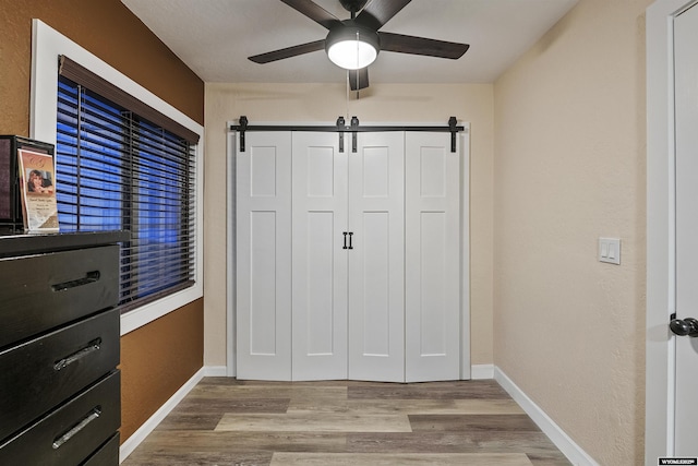 unfurnished bedroom with ceiling fan, a barn door, light hardwood / wood-style floors, and a closet