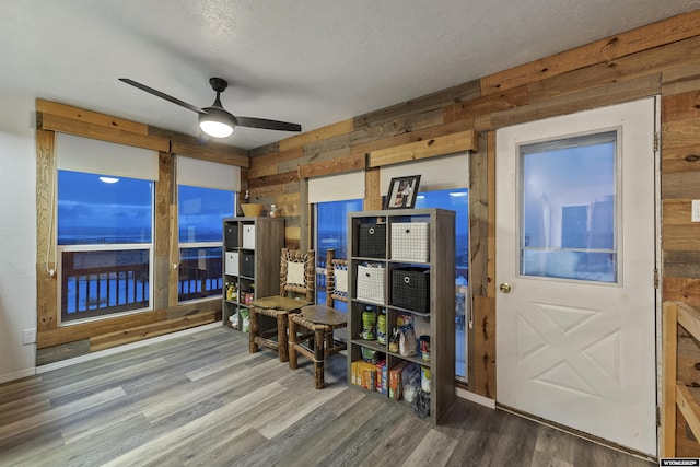 interior space with ceiling fan, wood-type flooring, wood walls, and a textured ceiling