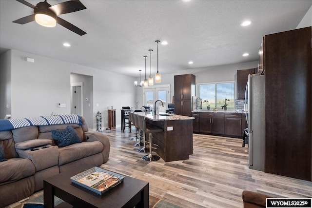 living area featuring ceiling fan with notable chandelier, a textured ceiling, recessed lighting, and light wood-style floors