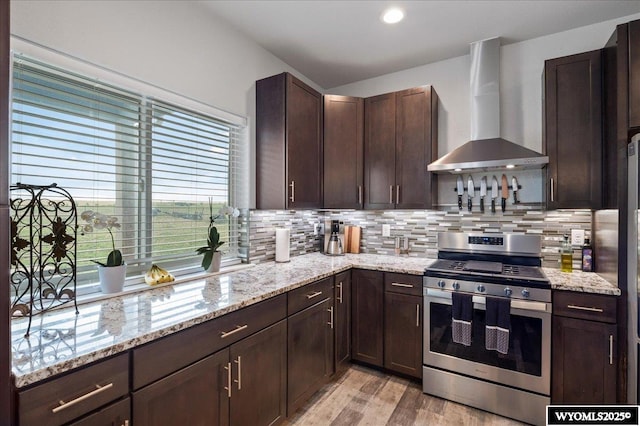 kitchen with wall chimney range hood, stainless steel range with gas cooktop, light stone counters, and decorative backsplash