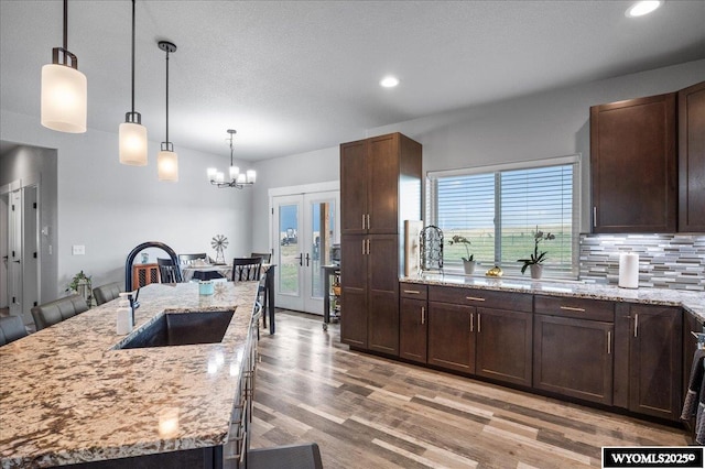 kitchen with pendant lighting, decorative backsplash, a kitchen island with sink, a sink, and light stone countertops