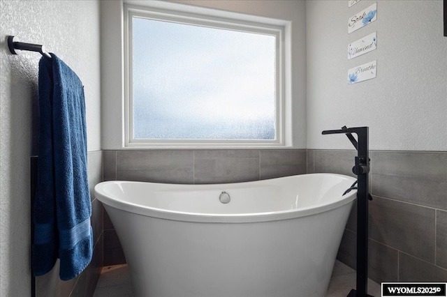 full bathroom with a freestanding tub, tile walls, and wainscoting