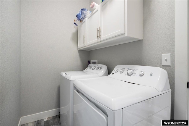 laundry room with a textured wall, wood finished floors, baseboards, cabinet space, and washing machine and clothes dryer