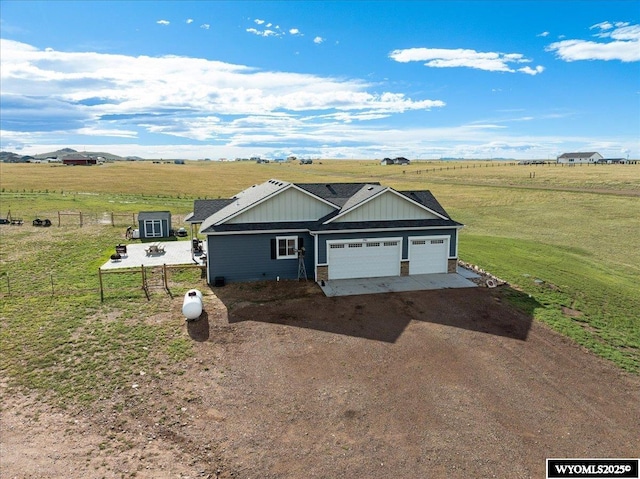 view of front of house with driveway, a garage, a rural view, fence, and board and batten siding