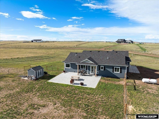 back of property with a storage shed, a patio, a rural view, fence, and an outdoor structure