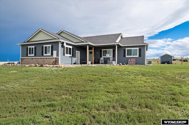 view of front of house with board and batten siding, stone siding, roof with shingles, and a front lawn