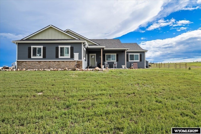 view of front of house featuring board and batten siding, a front yard, stone siding, and fence