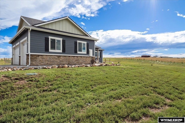 view of side of home with a garage, stone siding, a rural view, a yard, and board and batten siding