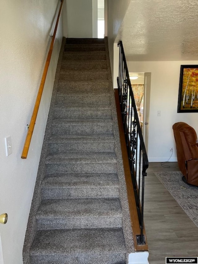 stairs featuring a textured ceiling, wood finished floors, and baseboards